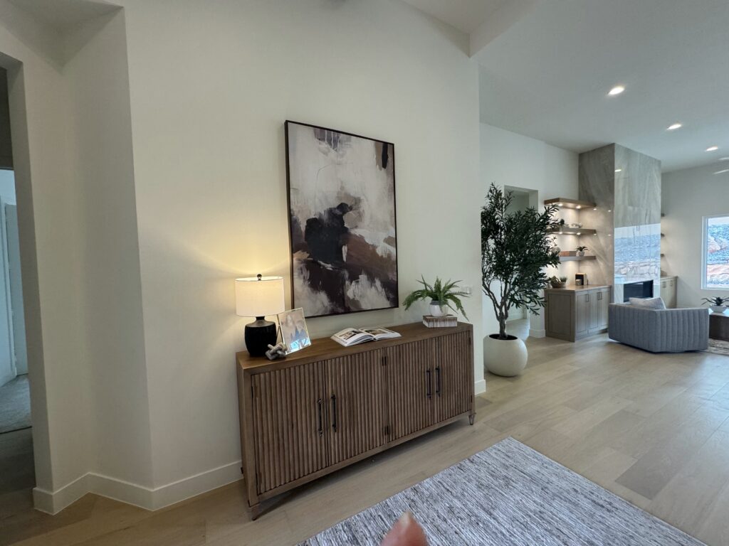 Professionally staged entryway console table with artwork, lamp, and decor leading into a modern open concept living room in a Southern Utah home